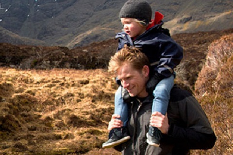 An image of father with child on his shoulders and a mountain background