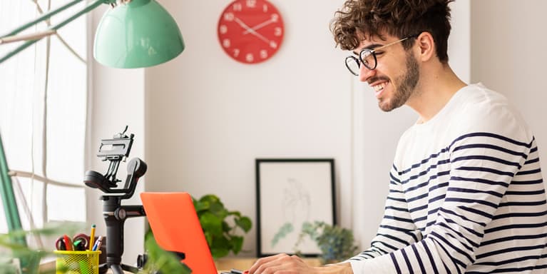 Young man on his laptop whilst sat at his home desk next to the window