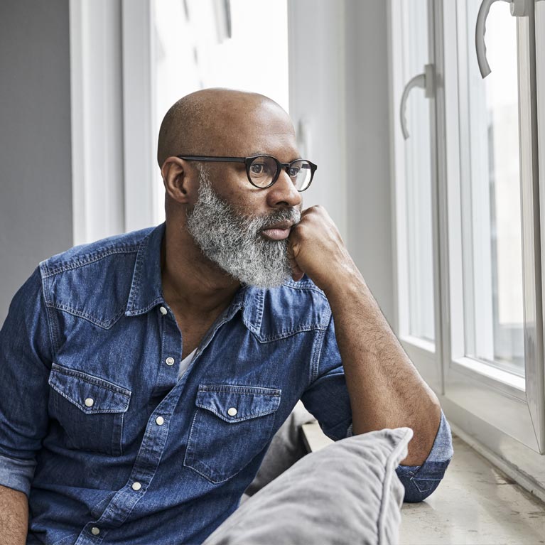 Man with beard and glasses looking out of window.