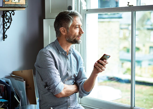 Man on a mobile device looking out of a window.