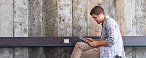 Photo of man sitting looking at tablet with a cup of coffee beside him